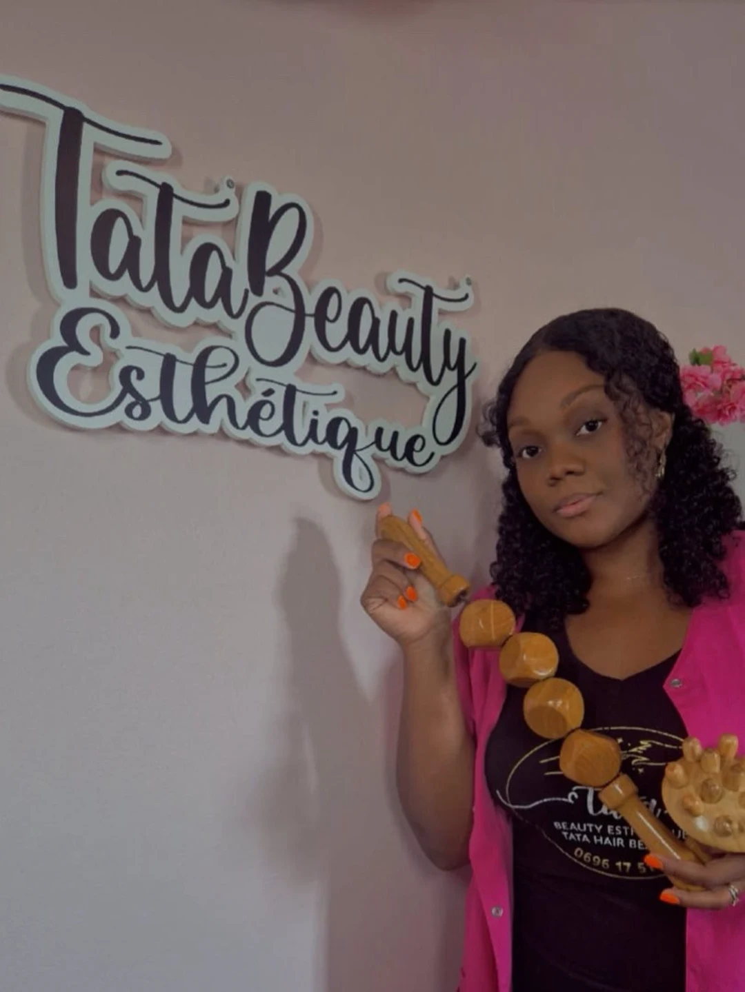 Tata, fondatrice, en tenue de studio devant l'enseigne murale Tata Beauty Esthétique